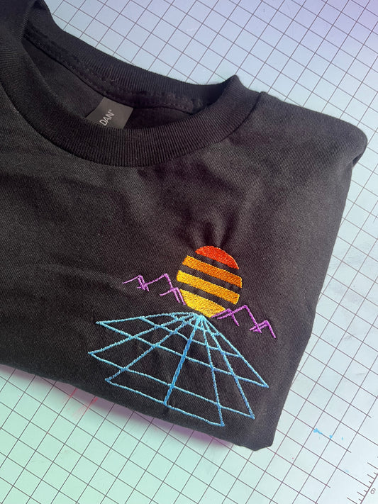 Black T-shirt with an embroidered design featuring a sunset with a purple mountain range and grid lines on a light blue background.